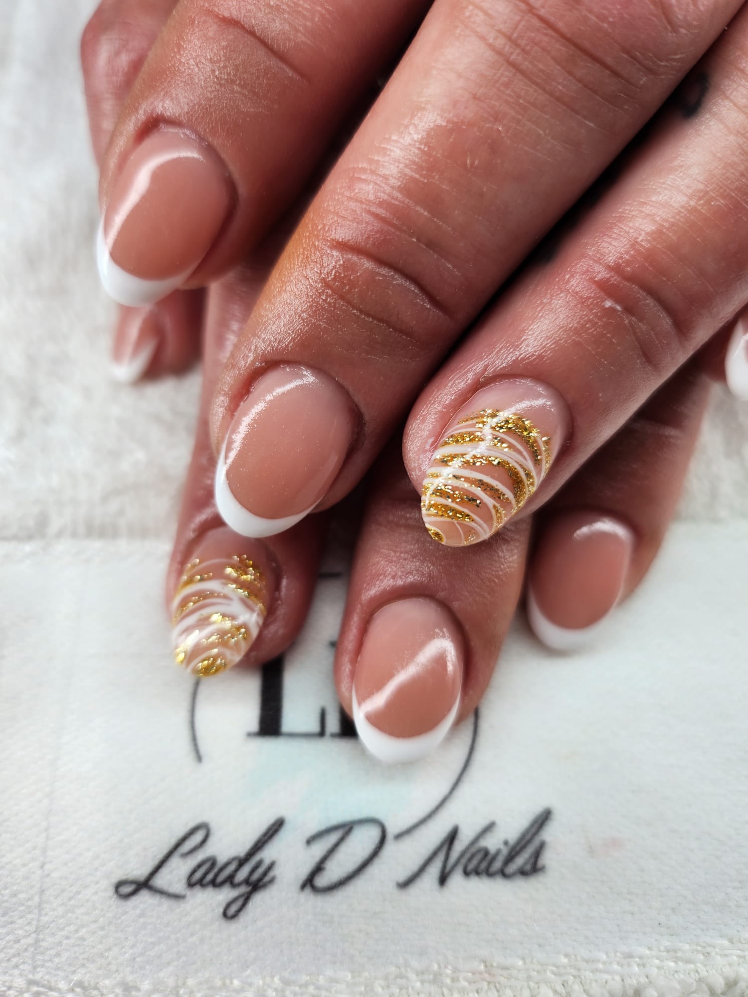Weisse French-Nägel mit goldenem Glitzer-Swirl auf zwei Akzentnägeln