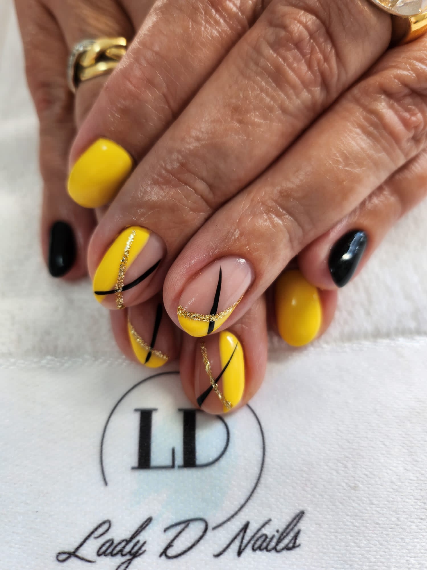 Gelbe Nägel mit schwarzen Linien und goldenem Glitzer